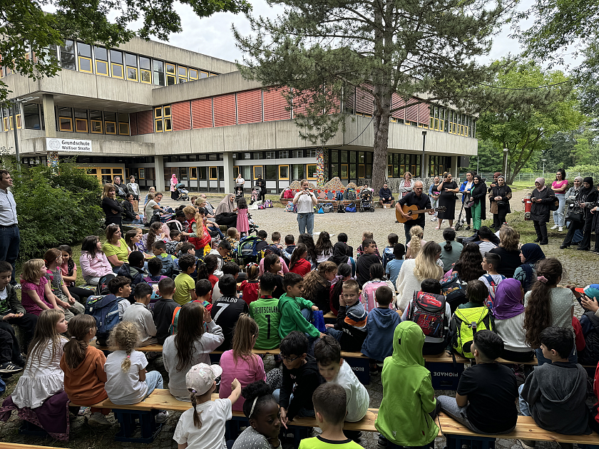 Kinder und Lehrkräfte singen vor dem Schulgebäude