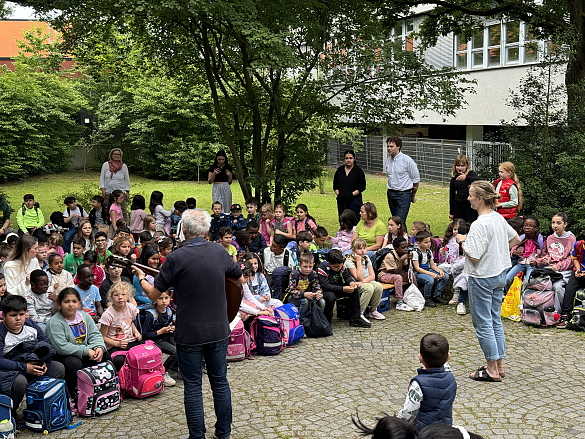 Kinder und Lehrkräfte singen vor dem Schulgebäude