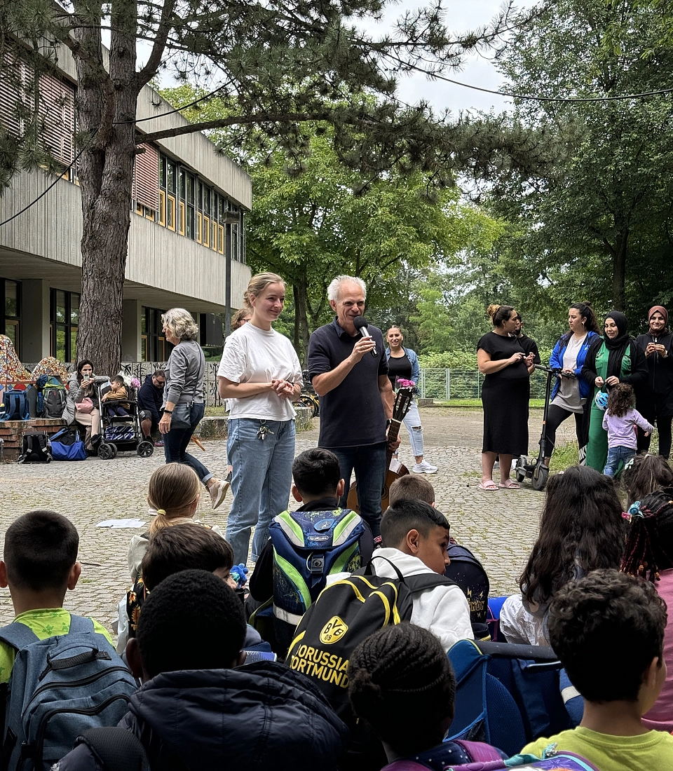 Kinder und Lehrkr&auml;fte singen vor dem Schulgeb&auml;ude