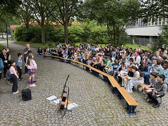 Die Schulgemeinschaft sitzt draußen bei der Bühne