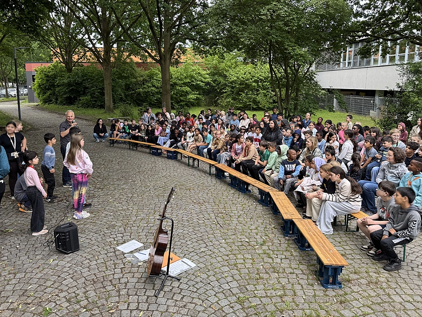 Die Schulgemeinschaft sitzt draußen bei der Bühne