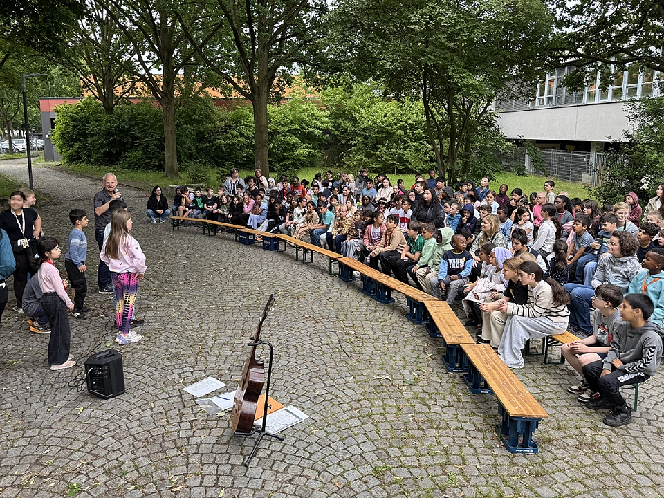 Die Schulgemeinschaft sitzt drau&szlig;en bei der B&uuml;hne