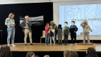 Frau Thielmann, Herr Leimbach und Frau Bahrenburg proben mit Kindern die Übergabe von Geschenken an ehrenamtliche Helfer:innen unserer Schule